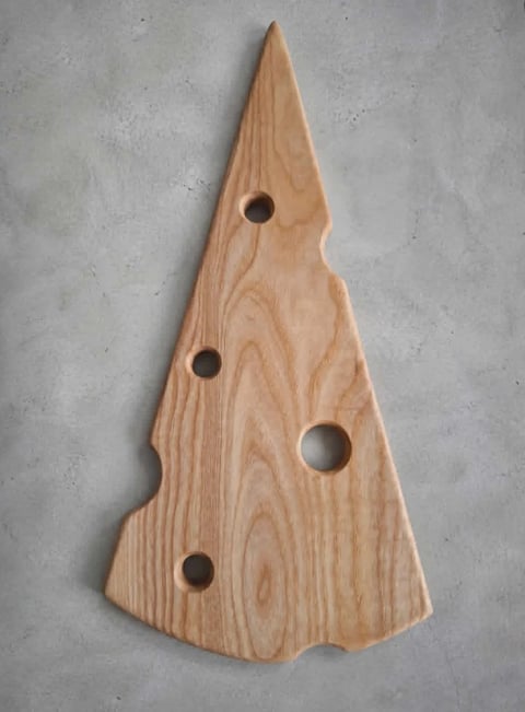 Wooden Christmas tree-shaped cutting board with four circular cutout handles on a gray textured background