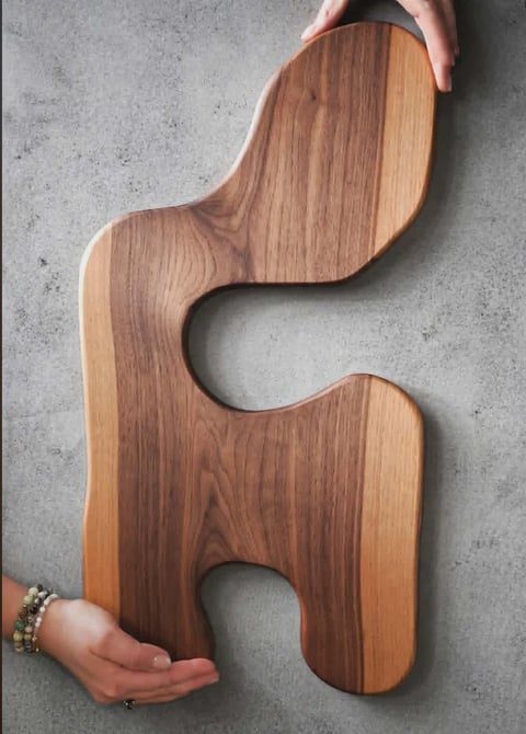 Person holding an interlocking wooden puzzle piece with curved edges against a concrete background
