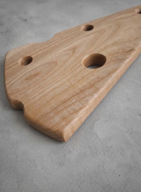 Wooden tool or decorative piece with rounded triangular shape and three circular holes, displayed on gray concrete surface