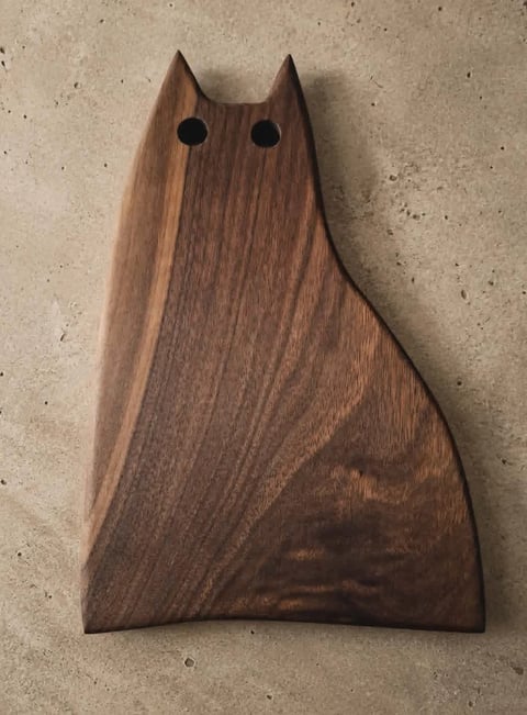 Wooden cat-shaped cutting board or serving board with pointed ears and black dot eyes on a concrete surface